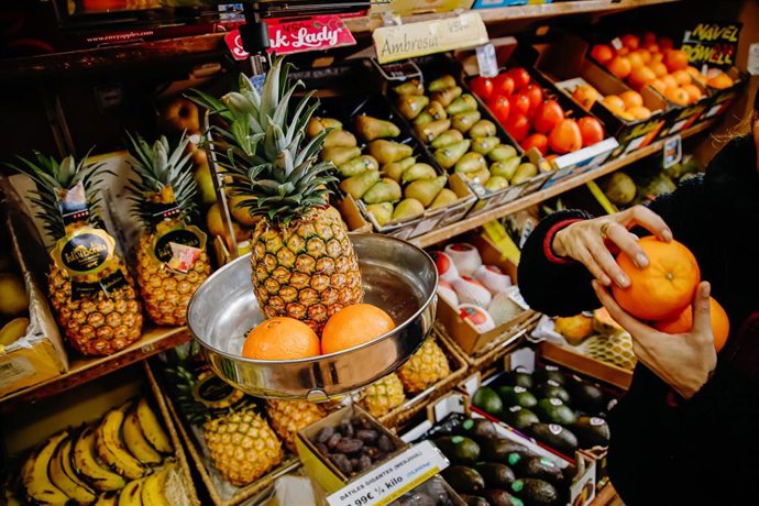 Archivo - Una persona pesa dos piezas de naranjas y una piña en la frutería 'Vitaminas', en Madrid (España).