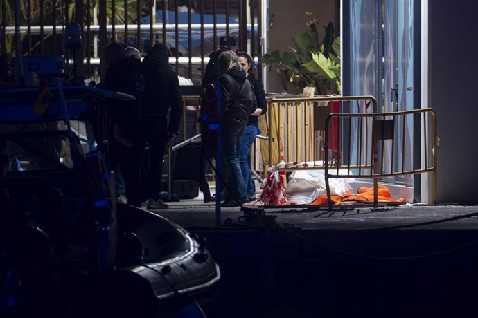 Varias personas junto al cadáver aparecido en la playa del Somorrostro de Barcelona