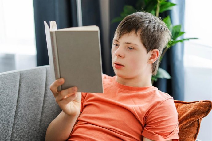 Archivo - Young man with down syndrome enjoying a book, comfortably sitting on a sofa at home, student studying. Knowledge concept, education