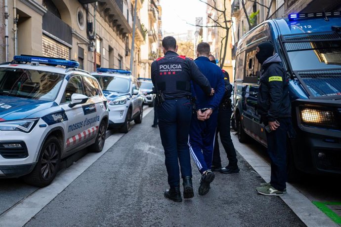 Un agente  de los Mossos d'Esquadra se lleva a un detenido durante un operativo policial contra el tráfico internacional de armas y drogas, a 23 de marzo de 2026, en Barcelona, Catalunya (España). 