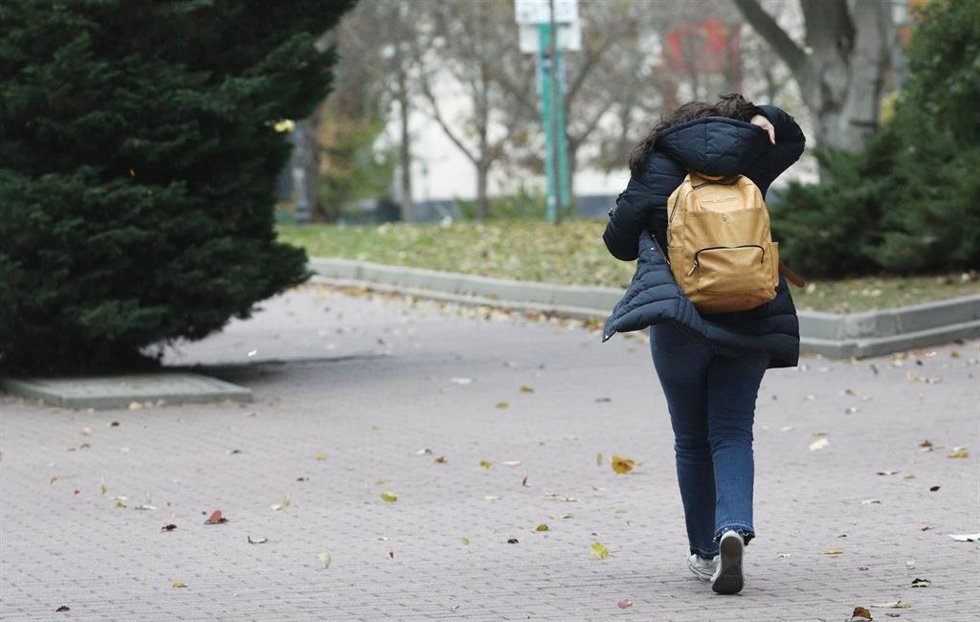Archivo - Una mujer caminando por la calle se protege del viento