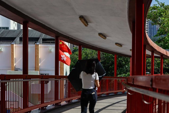 Archivo - October 1, 2023, Hong Kong, Hong Kong, China: A woman walks on a footbridge near a Hong Kong SAR flag and  Chinese national flag, on the 74th anniversary of the founding of the People's Republic of China are seen at the mailboxes inside a reside