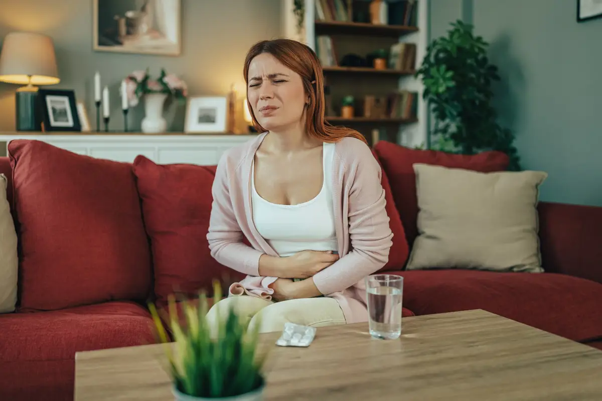 Mujer sentada en el sofá con dolor de estómago