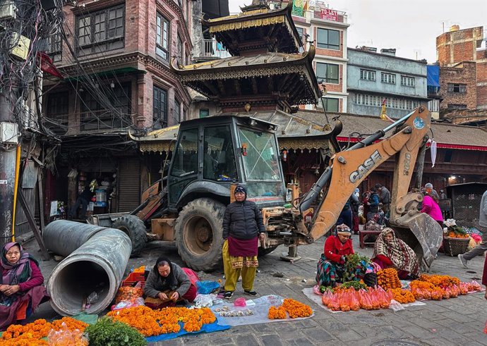 Archivo - December 16, 2025, Kathmandu, Nepal: Women flower vendors continue their trade in front of a bulldozer brought for alley excavation at Ason Market in Kathmandu, Nepal, on December 16, 2025.