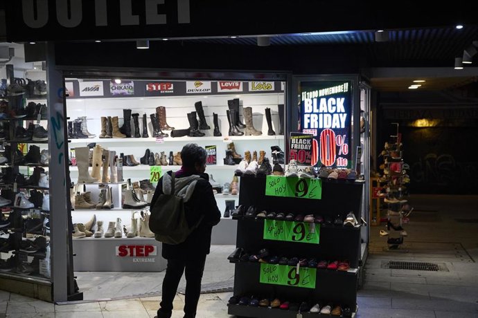 Archivo - Personas delante de un comercio anunciando descuentos por el Black Friday