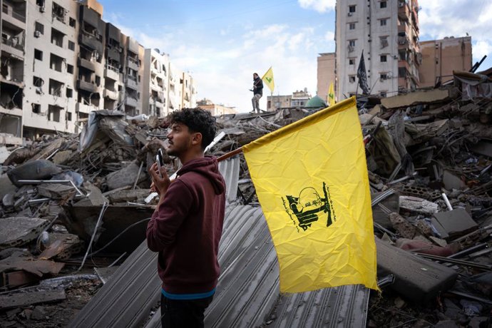 Archivo - Arquivo - 27 de novembro de 2024, Dahiye, Líbano: Dois homens seguram bandeiras do Hezbollah sobre as ruínas de um prédio bombardeado. Às 4h da manhã, horário local, o cessar-fogo entre Israel e o Hezbollah entrou em vigor após meses de intensos