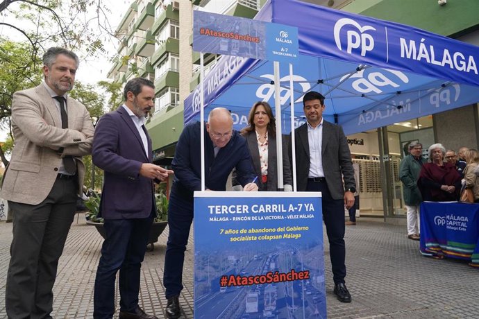 El secretario general del PP, Miguel Tellado (c), y la presidenta del PP de Málaga, Patricia Navarro (2d), junto a una pancarta para reclamar un tercer carril en la A-7 de Málaga. 