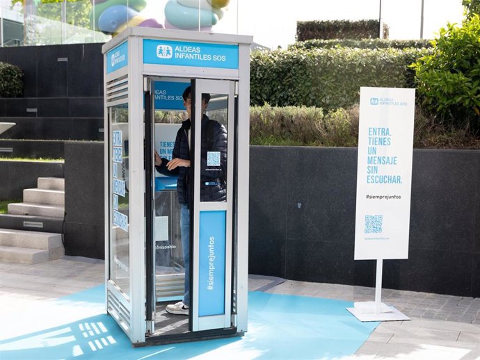 Una persona dentro de la cabina telefónica de Aldeas Infantiles SOS durante una acción-protesta, en el Centro de ocio Caleido.