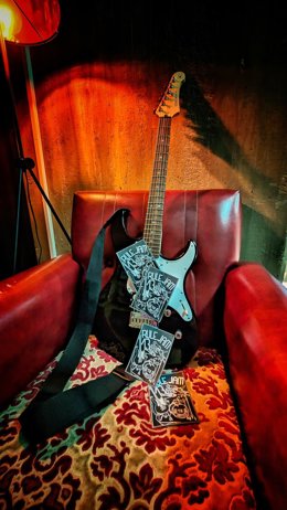Imagen de recurso de una guitarra eléctrica descansa sobre una butaca roja junto a varios folletos informativos de la iniciativa 'RULE JAM'