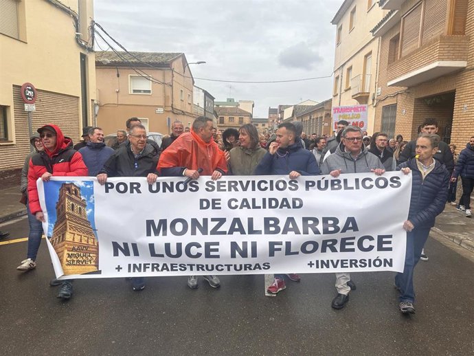 La portavoz socialista en el Ayuntamiento de Zaragoza, Lola Ranera, y el alcalde de Monzalbarba, Joaquín Tiestos, al frente de una pancarta  durnate la manifestación de protesta de este domingo en el barrio rural zaragozano para reclamar mejoras.