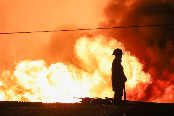 Archivo - Un bombero en una azotea mientras intenta extinguir un enorme incendio que arrasa las chabolas de un barrio marginal de Quezón, Filipinas