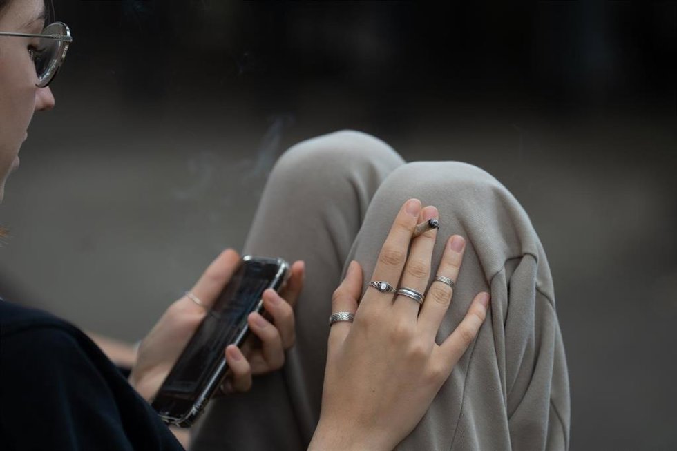 Archivo - Una joven fuma y lee su movil 