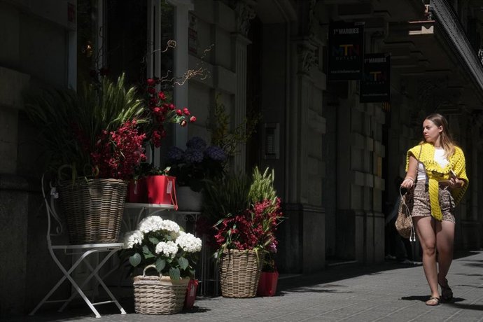 Una chica pasa por delante de una floristería mirando las rosas expuestas en la puerta