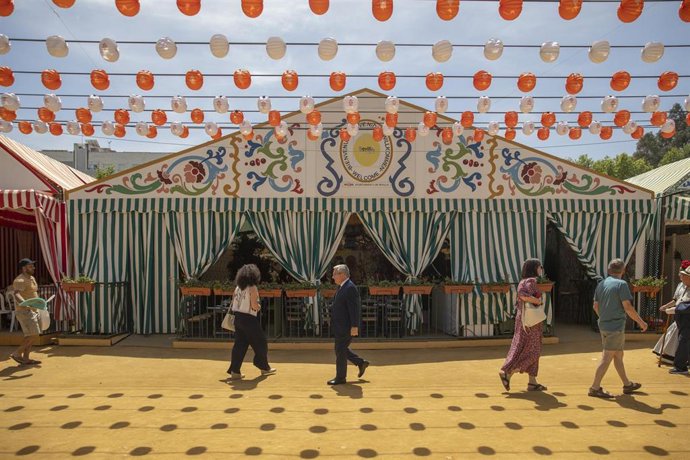Archivo - Varias personas pasan por delante de la caseta de los turistas en la feria. 