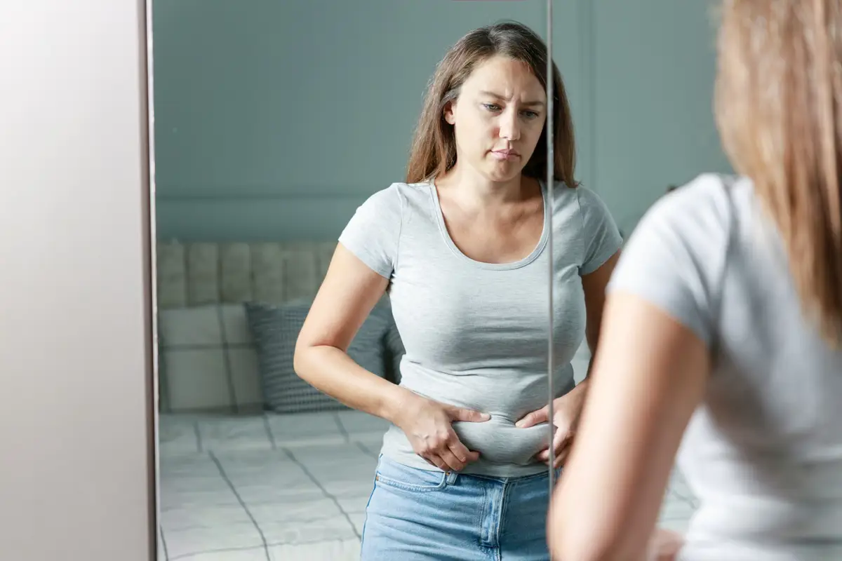 Mujer mirándose en el espejo preocupada por su barriga.