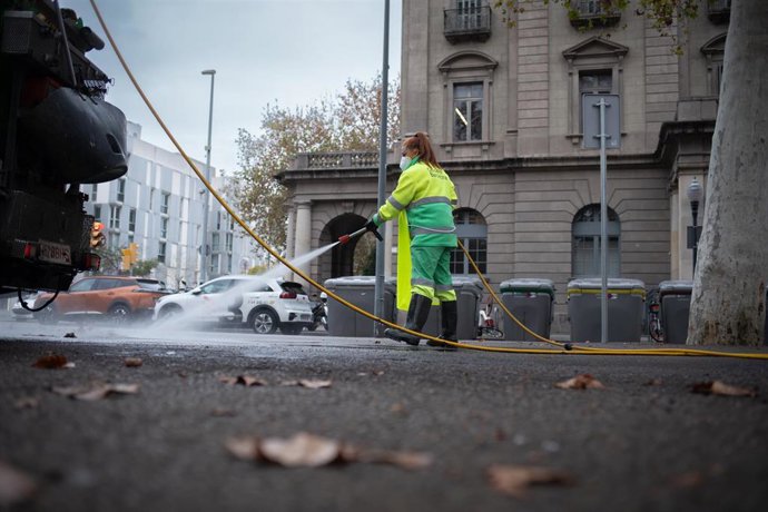 Archivo - Una trabajadora de la limpieza riega una calle con una manguera en Barcelona