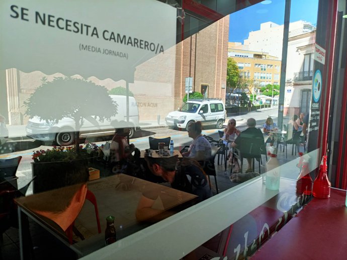 Cartel de 'Se busca camarero' en un bar con terraza.