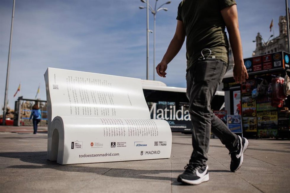 Archivo - Dos personas camina frente a un banco con forma de libro de la campaña ‘Asienta la lectura-siéntate a leer’, en el Paseo del Prado, a 20 de marzo de 2023, en Madrid (España).