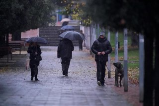 Archivo - Ciudadanos caminan mientras llueve