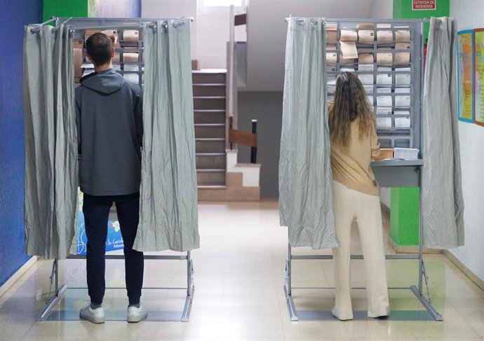 Archivo - Dos personas ejercen su derecho a voto en una cabina en un colegio electoral.