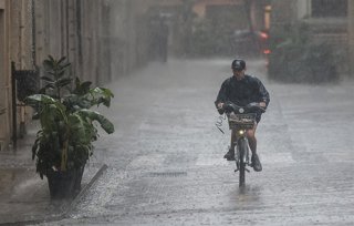 Archivo - Arxiu - Una persona amb bicicleta baix la pluja, en imatge d'arxiu. 
