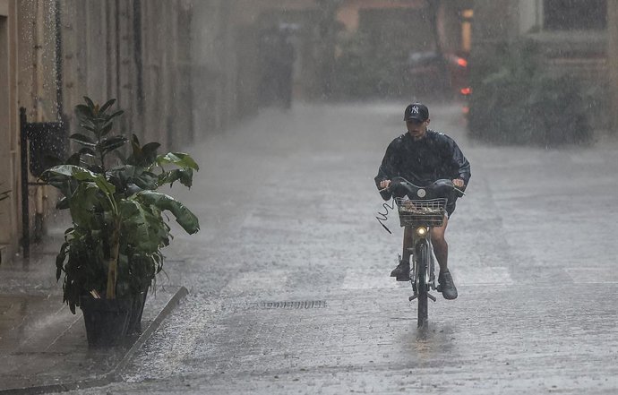 Archivo - Arxiu - Una persona amb bicicleta baix la pluja, en imatge d'arxiu. 