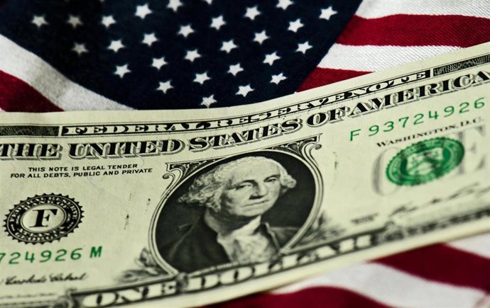 Archivo - Billete de un dólar junto a la bandera de Estados Unidos.
