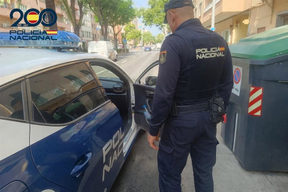 Archivo - Agente de la Policía Nacional frente a un coche patrulla.