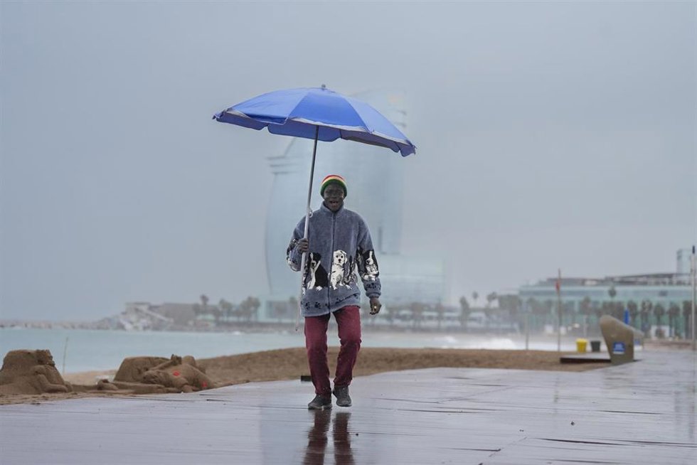 Archivo - Vecinos de Barcelona pasean bajo la lluvia en la playa de la Barceloneta durante el temporal, a 19 de enero de 2026, en Barcelona