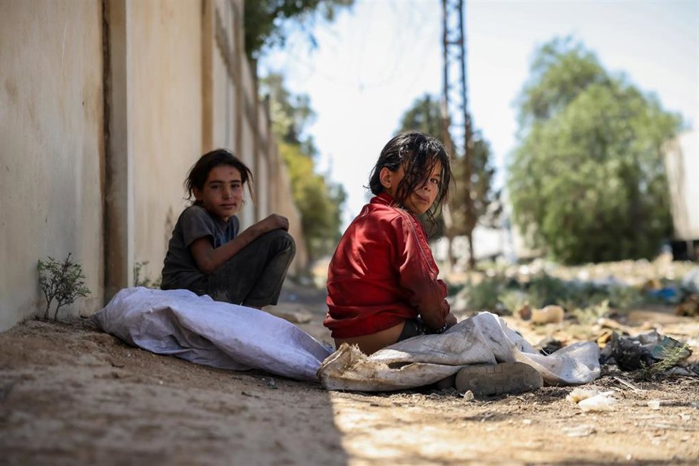 Archivo - Dos niñas sirias con ropas desgastadas descansan al borde de la carretera después de rebuscar entre la basura restos de plástico para vender y ayudar a mantener a su familia, en Damasco  