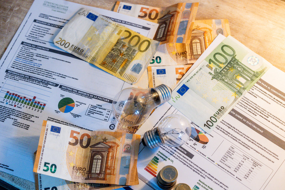 Dos bombillas sobre billetes, monedas y facturas en imagen de archivo