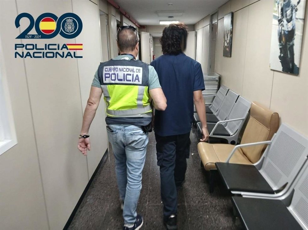 Uno de los arrestados, de espaldas, escoltado por un agente de la Policía Nacional.