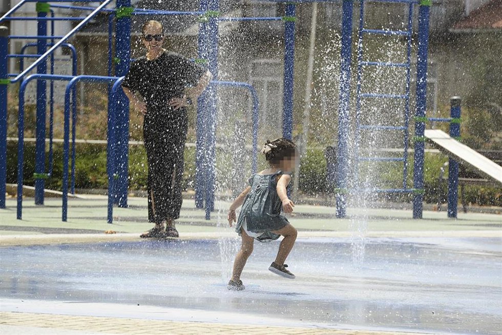 Archivo - Dos personas se refrescan en unos chorros en un día caluroso.