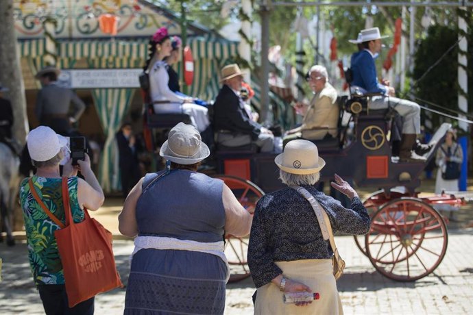 Archivo - Turistas pasean por el Real de la Feria ataviados con gorros para protegerse del Sol en imagen de archivo.