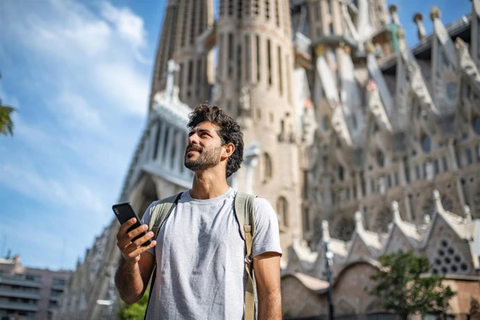 Archivo - Vista de un  turista hispano de 30 años usando un teléfono inteligente como guía turística, con la Sagrada Familia de fondo