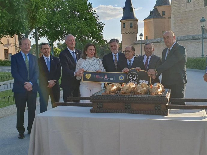 La consejera González Corral y el hostelero José María Ruiz (centro) sujetan una muestra de vitola ante varios cochinillos asados, junto a Autoridades asistentes al acto.