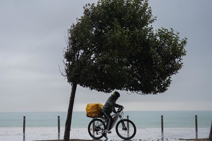 Archivo - Un home amb bicicleta sota la pluja