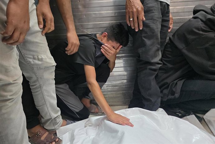 Palestinos junto a los cadáveres de dos personas muertas en un bombardeo de Israel contra el sur de la Franja de Gaza a pesar del alto el fuego pactado en octubre de 2025