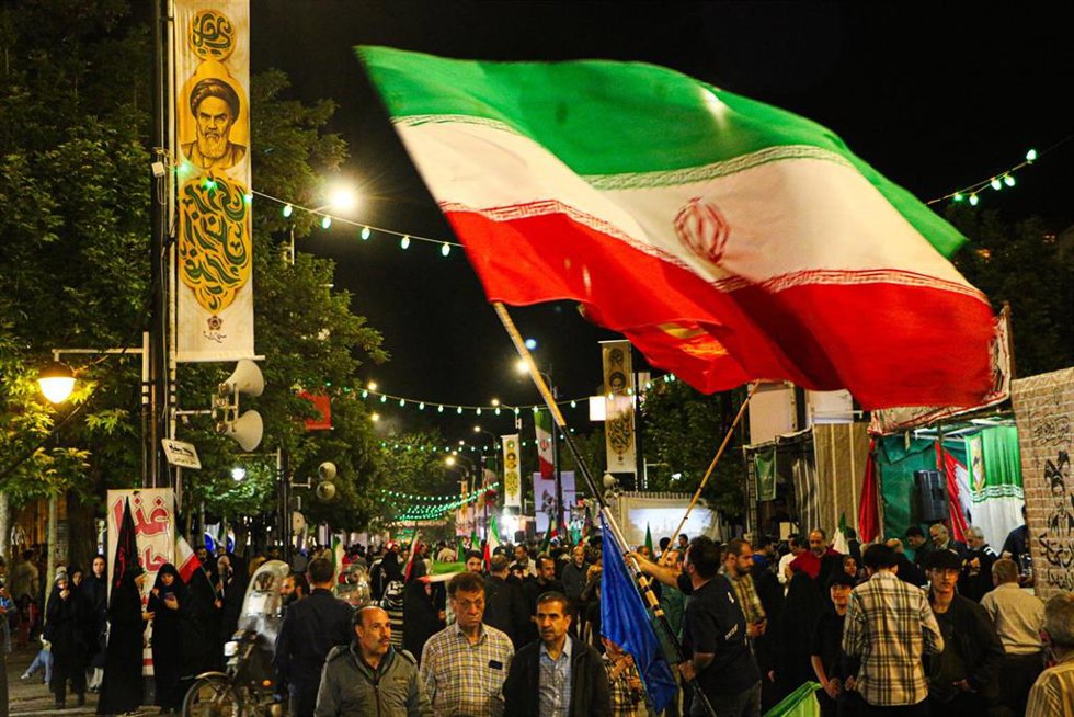 Manifestantes agitan una bandera nacional iraní sobre la multitud durante una concentración organizada por el Estado en Irán