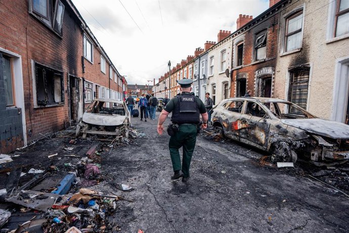 Agente de policía inspeccionando coches y edificios calcinados en la zona de Templemore tras las protestas violentas por el apuñalamiento de un hombre de Belfast Norte. 