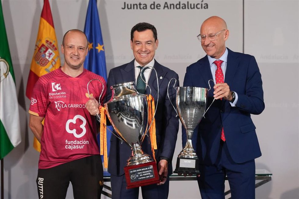 El presidente en funciones de la Junta de Andalucía, Juanma Moreno (c), junto al capitán y el presidente del Real Priego TM, Carlos Machado (i) y Jesús Machado (d), durante la recepción en San Telmo, con las copas de liga y de Europa.