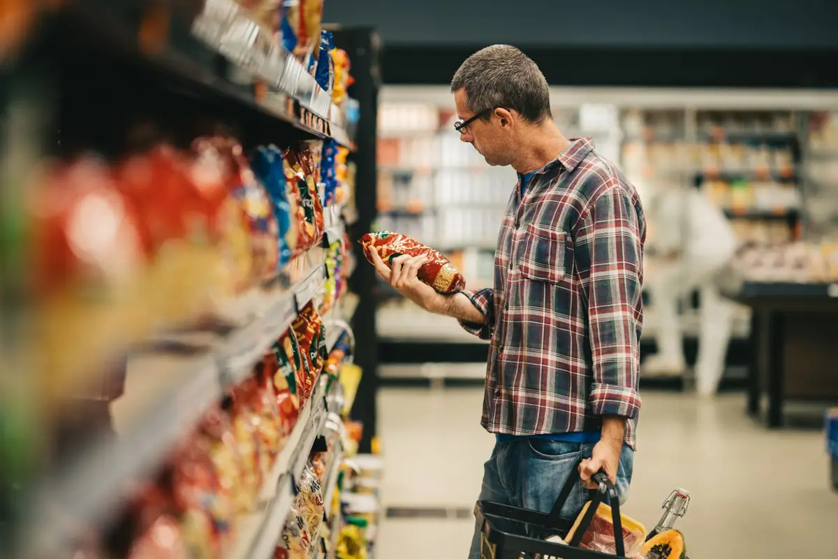 Hombre examinando la etiqueta de los alimentos mientras hace la compra en un supermercado. - GISELLEFLISSAK/ISTOCK - Archivo