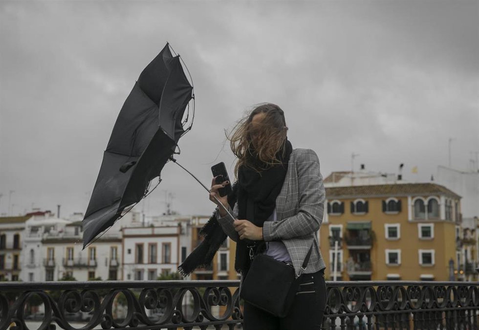 Archivo - Una racha de viento desbarata el paragüas de una viandante mientras camina por el Puente de Isabel II de Sevilla.