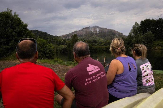 Varias personas observan las columnas de humo durante las labores de extinción de un incendio forestal, a 14 de junio de 2026, en Grado, Asturias (España). 