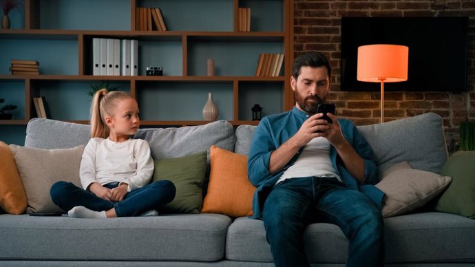 Archivo - Padre joven usando el teléfono móvil. La niña necesita atención mientras su padre usa un dispositivo moderno. Concepto de adicción a la tecnología de internet en la generación joven