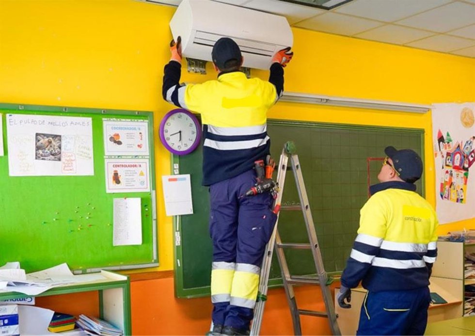 Un operario instala un split de aire acondicionado en un aula.E