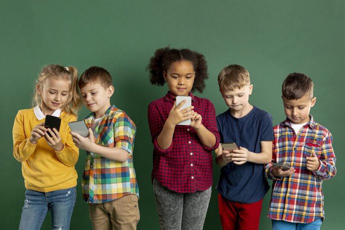 Archivo - Un grupo de niños utilizando teléfonos móviles.