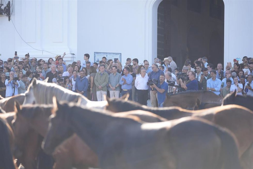 El presidente en funciones de la Junta de Andalucía, Juanma Moreno (al fondo, en la puerta de la ermita con camisa gris), asiste a la Saca de las Yeguas de Almonte.