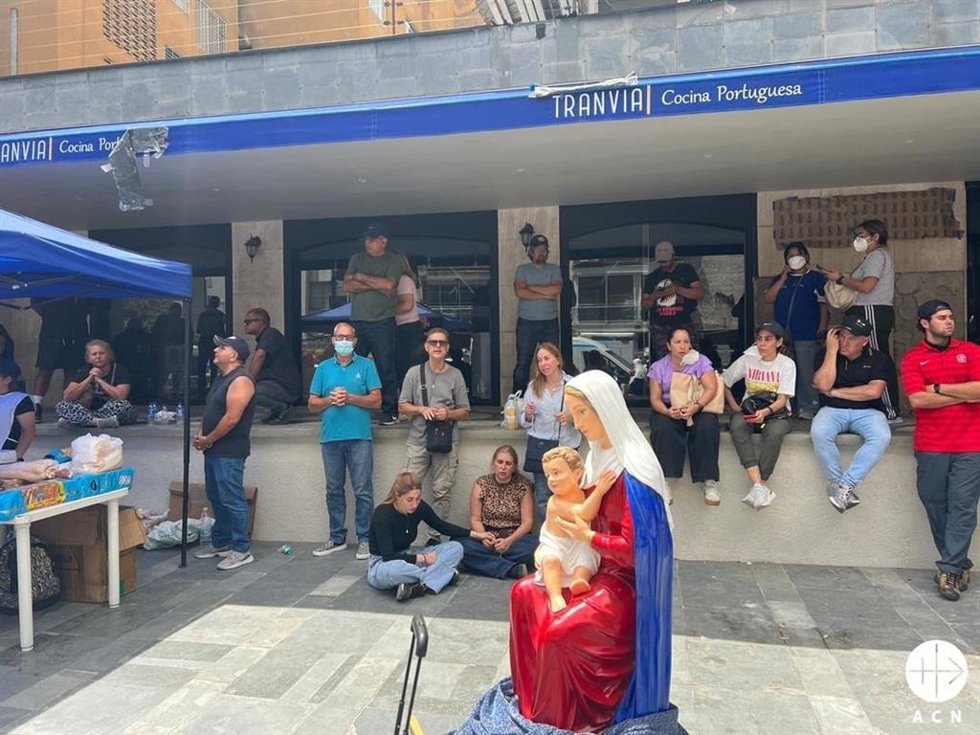 Personas en la calle en Caracas, rezando juntas en torno a una imagen de la Virgen y junto a un puesto de ayuda de la Iglesia católica.