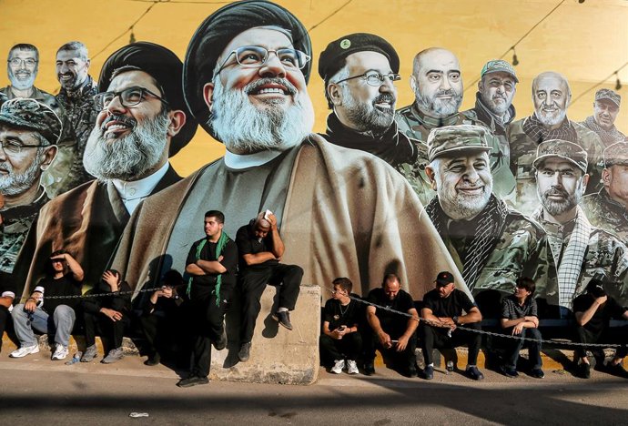 26 de junho de 2026, Beirute, Líbano: Apoiadores do Hezbollah, grupo pró-iraniano, sentam-se em frente a um cartaz dos líderes do partido assassinados por Israel no subúrbio sul de Beirute, enquanto prestam homenagem durante o último dia da Ashura, que ma